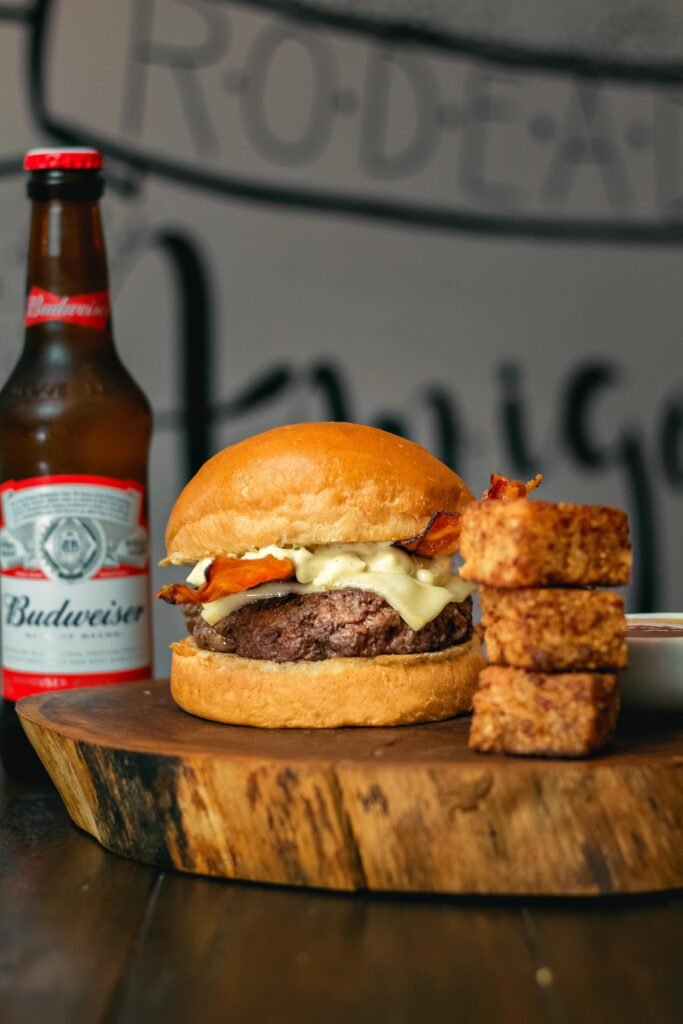 Delicious gourmet burger paired with a Budweiser beer and crispy appetizers on a wooden board.